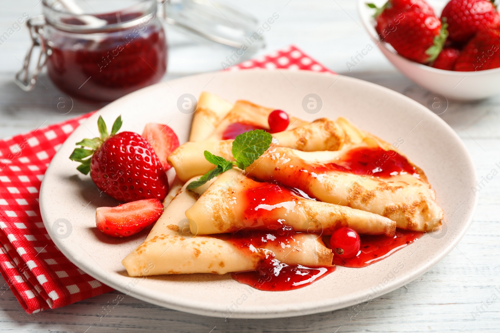 Photo of Delicious thin pancakes with strawberries and jam on white wooden table