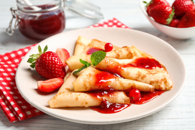Photo of Delicious thin pancakes with strawberries and jam on white wooden table