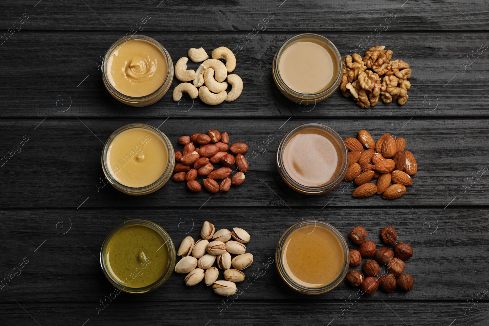 Photo of Jars with butters made of different nuts and ingredients on black wooden table, flat lay