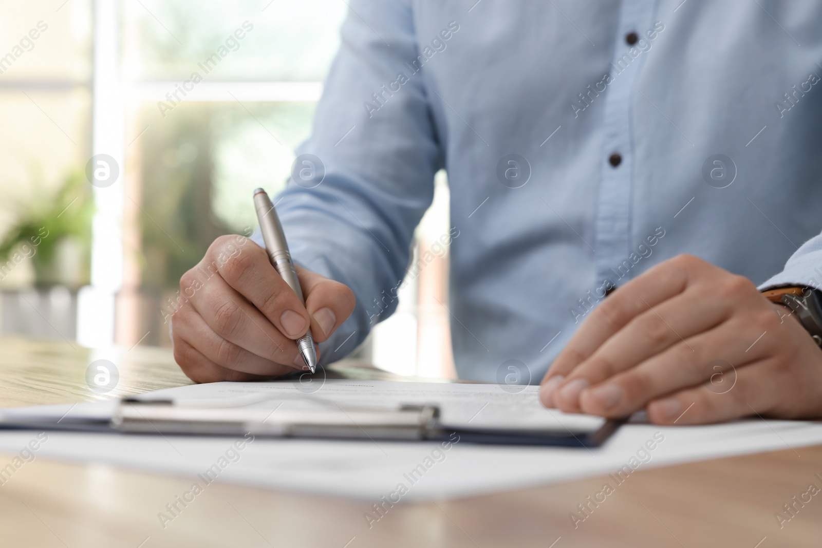 Photo of Man signing contract at table in office, closeup.