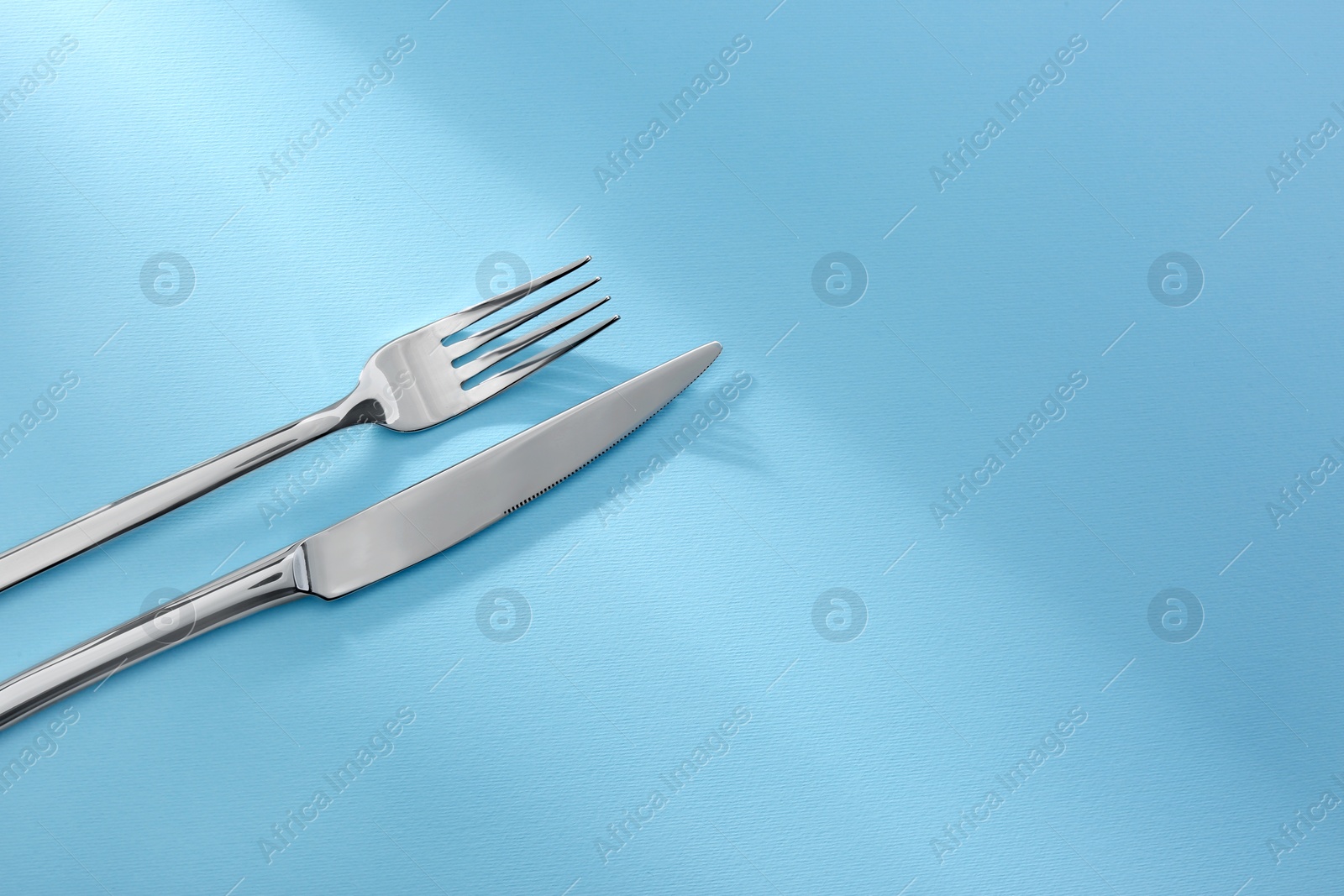 Photo of Shiny fork and knife on light blue background. Space for text
