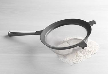 Sieve and flour on white wooden table