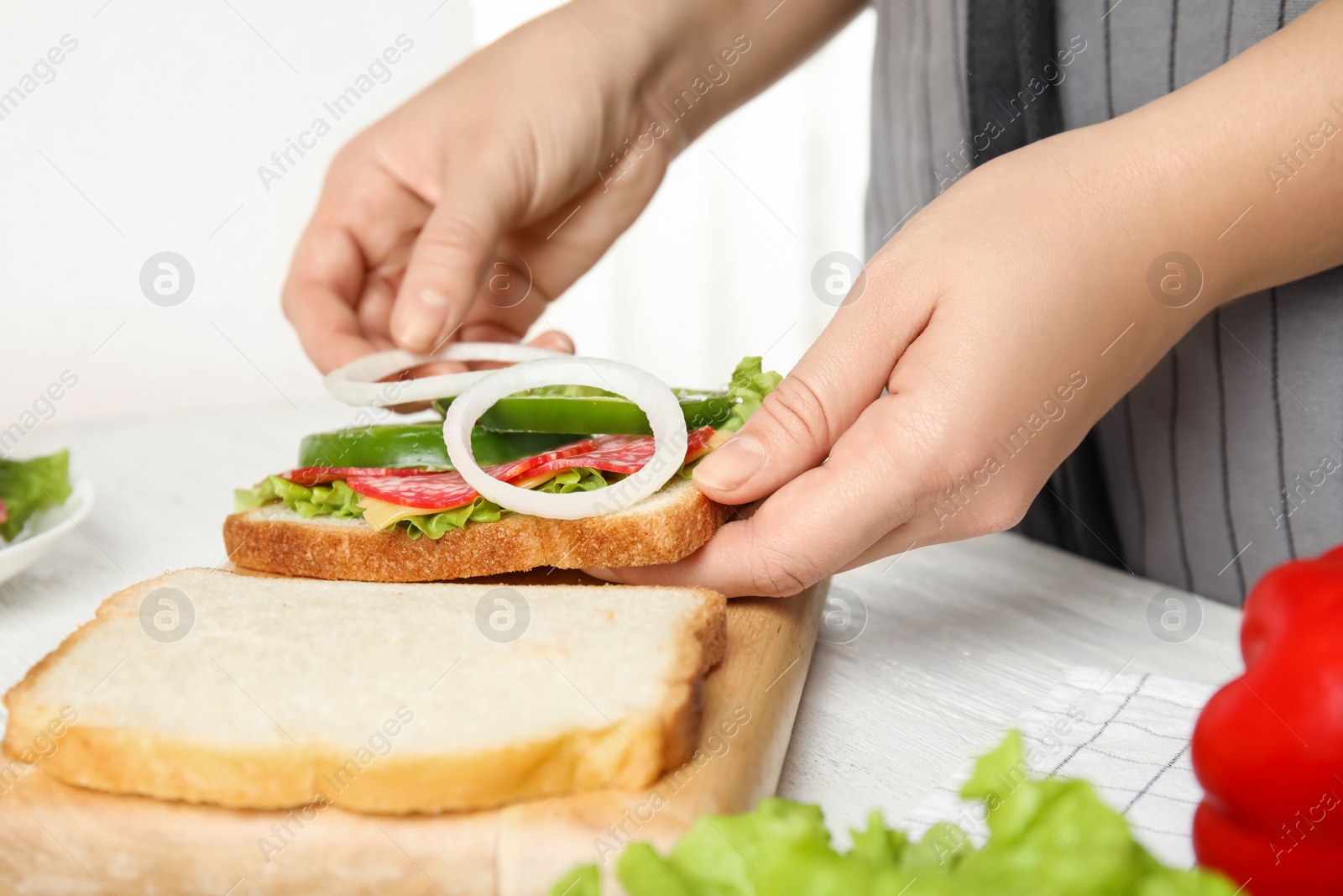 Photo of Woman adding onion to tasty sandwich at white wooden table, closeup