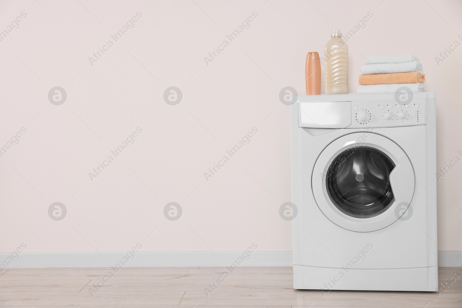 Photo of Modern washing machine, folded towels and bottles near white wall indoors. Space for text