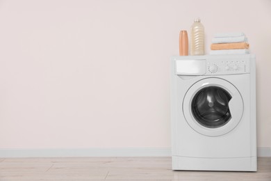 Photo of Modern washing machine, folded towels and bottles near white wall indoors. Space for text