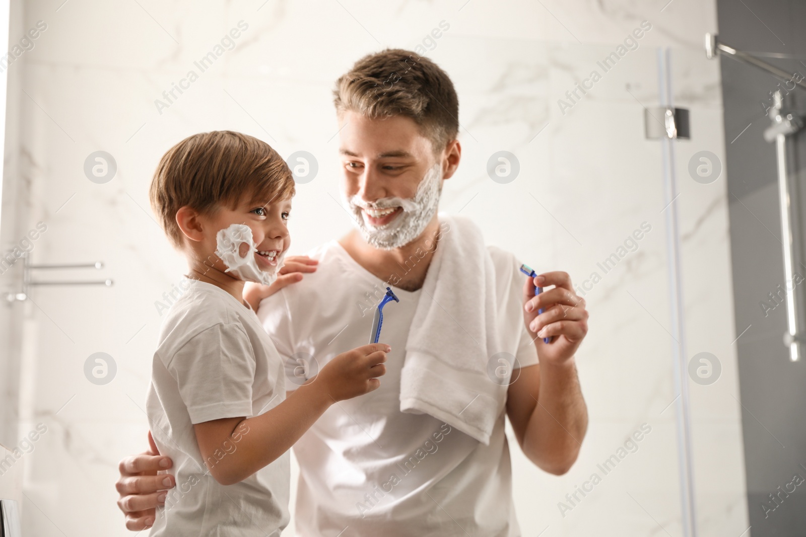 Photo of Dad and son with shaving foam on their faces having fun in bathroom