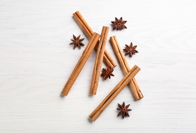 Aromatic cinnamon sticks and anise on white wooden table, flat lay