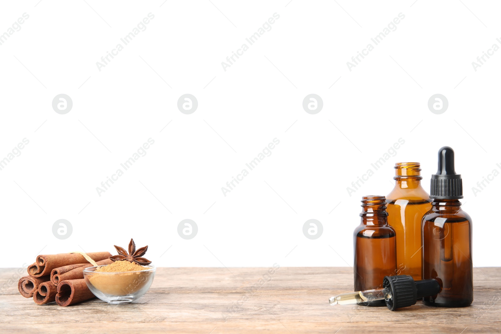 Photo of Bottles of essential oils, cinnamon sticks and powder on wooden table against white background. Space for text