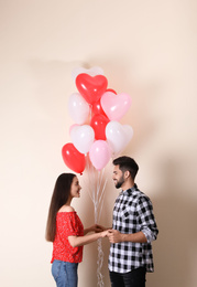 Photo of Beautiful couple with heart shaped balloons on beige background. Valentine's day celebration