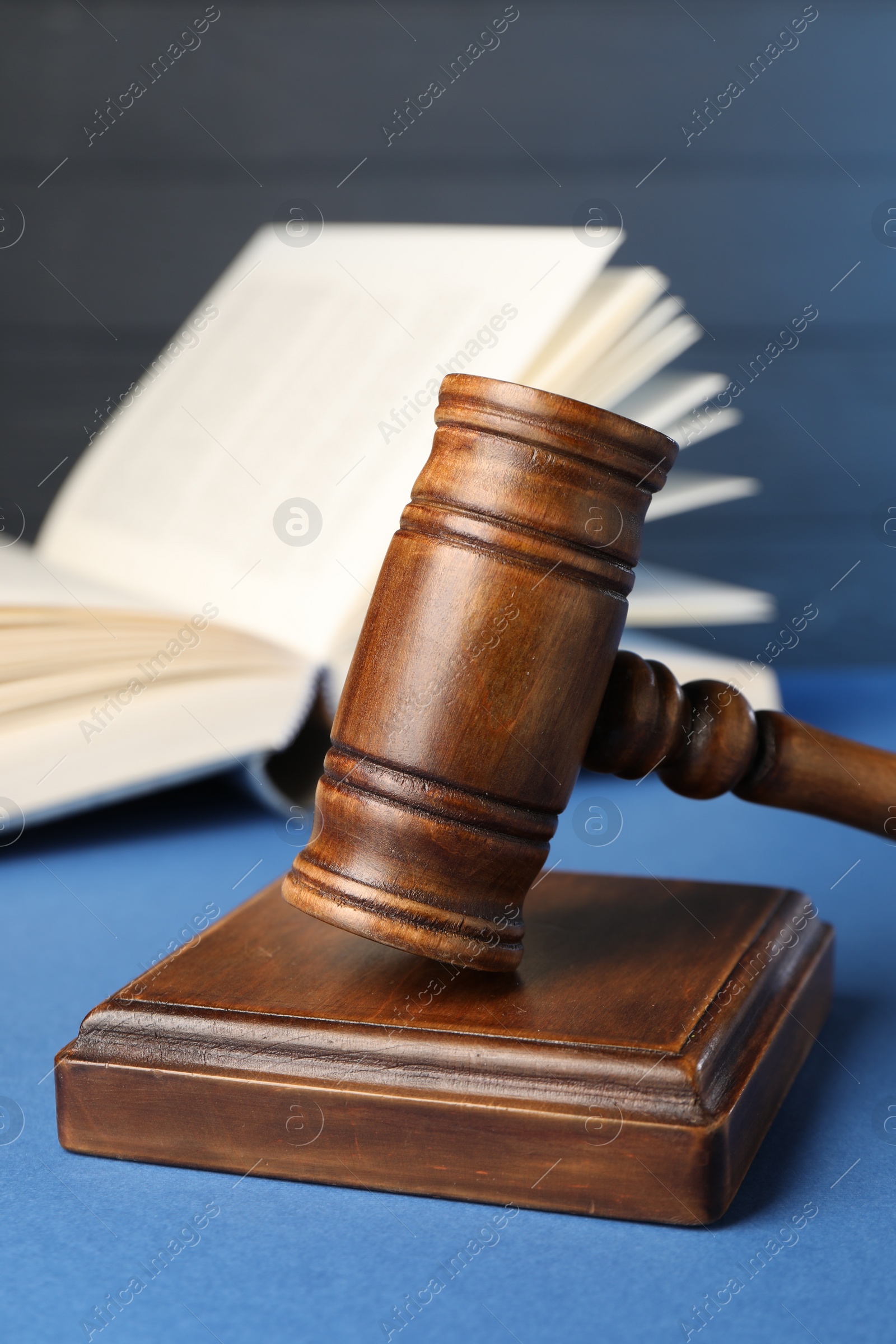 Photo of Wooden gavel, sound block and book on blue table, closeup