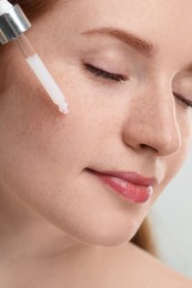 Beautiful woman with freckles applying cosmetic serum onto her face, closeup