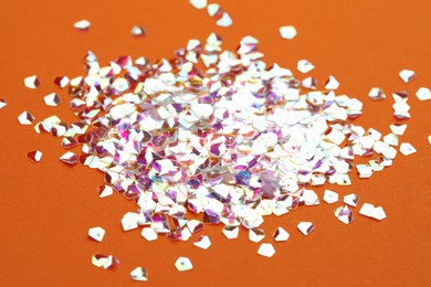 Photo of Pile of shiny glitter on orange background, closeup