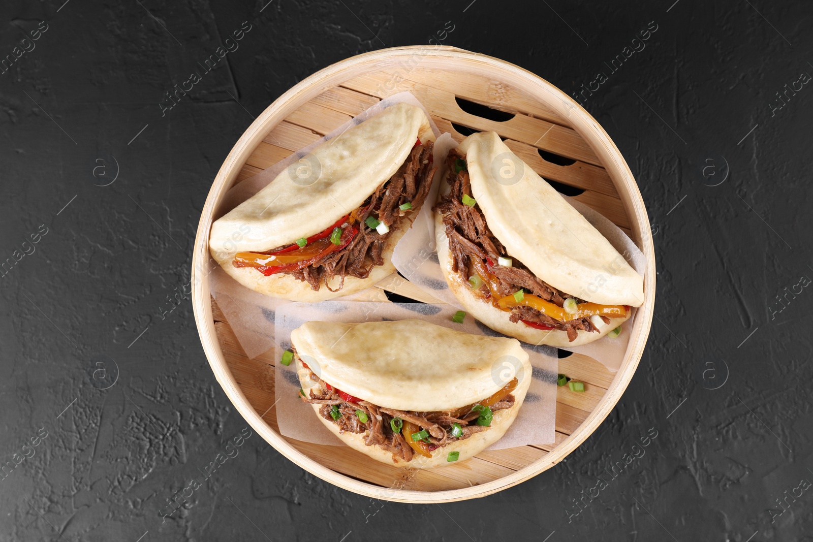 Photo of Delicious gua bao in bamboo steamer on black table, top view