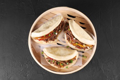 Delicious gua bao in bamboo steamer on black table, top view