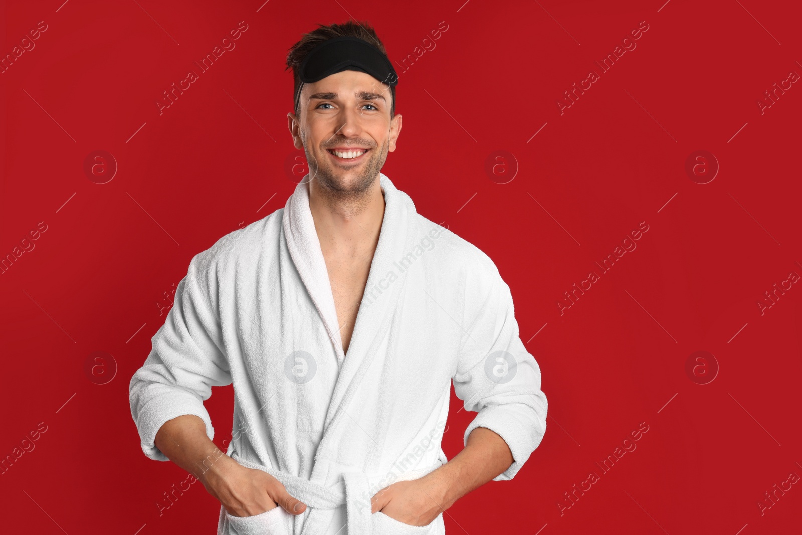 Photo of Happy young man in bathrobe on red background