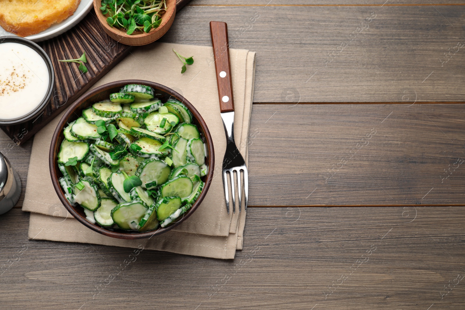 Photo of Bowl of delicious cucumber salad served on wooden table, flat lay. Space for text