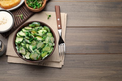 Bowl of delicious cucumber salad served on wooden table, flat lay. Space for text