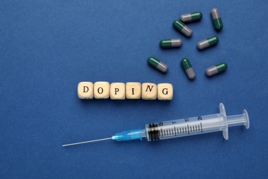 Photo of Wooden cubes with word Doping and drugs on blue background, flat lay