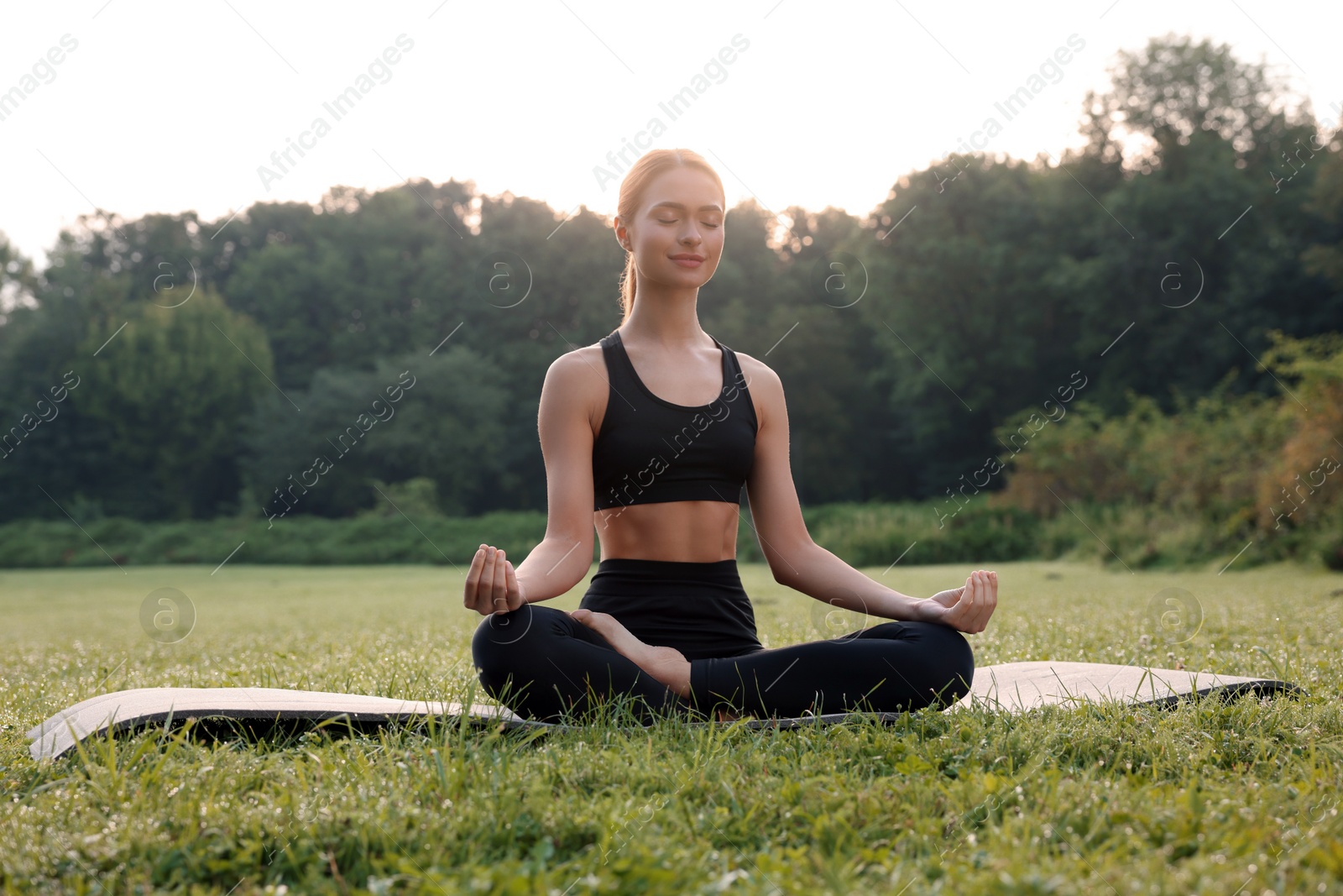 Photo of Beautiful young woman practicing Padmasana on yoga mat outdoors. Lotus pose