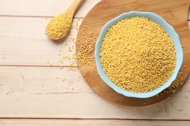 Millet groats in bowl and spoon on light wooden table, flat lay. Space for text