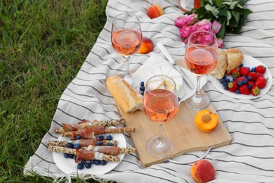 Glasses of delicious rose wine, flowers and food on picnic blanket outdoors