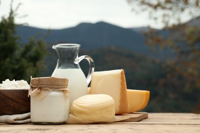 Photo of Tasty cottage cheese and other fresh dairy products on wooden table in mountains