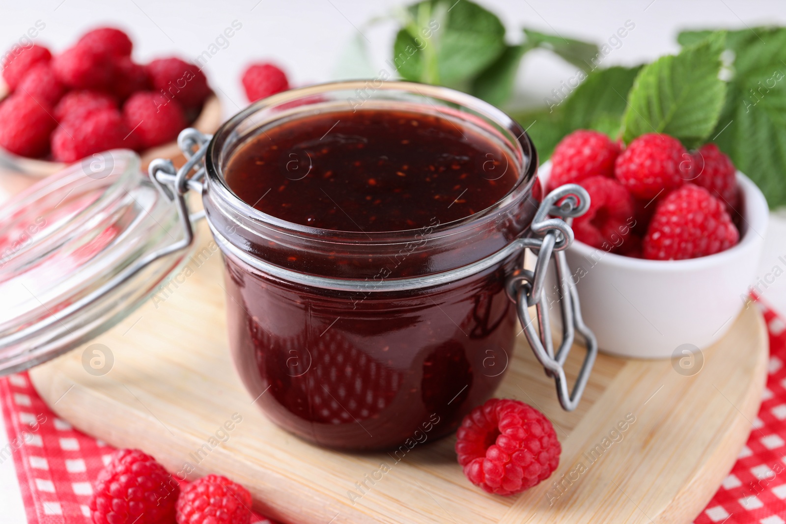 Photo of Jar of delicious raspberry jam and fresh berries on table, closeup
