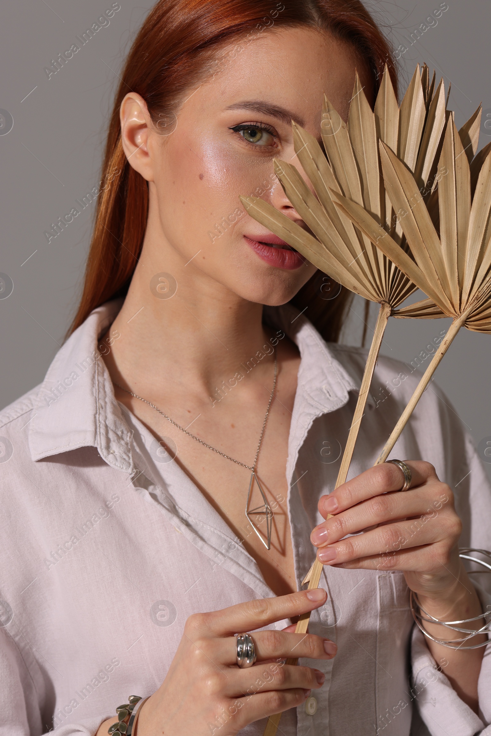 Photo of Beautiful young woman with elegant jewelry and decorative leaves on gray background