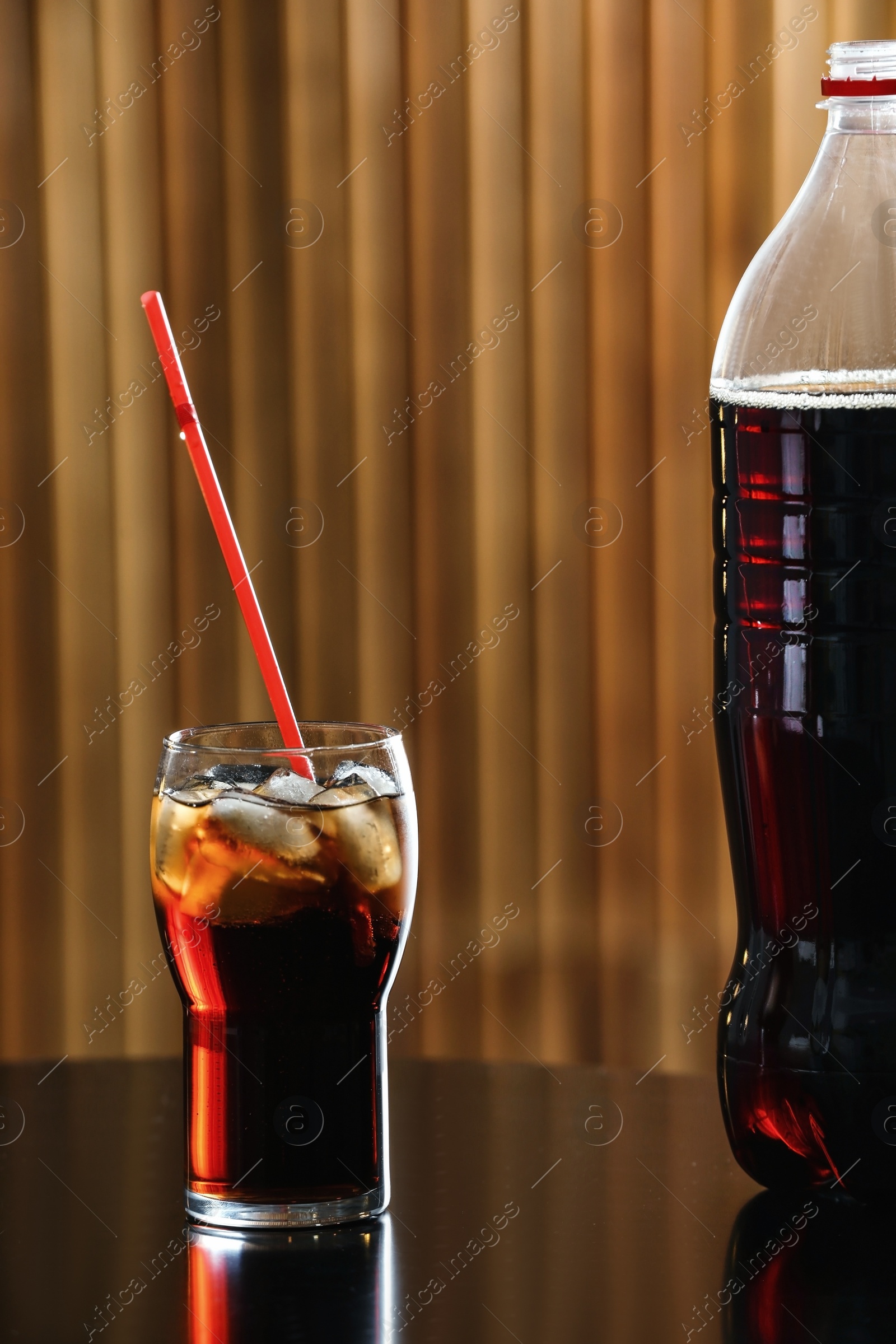 Photo of Glass of cola with ice on table against blurred background