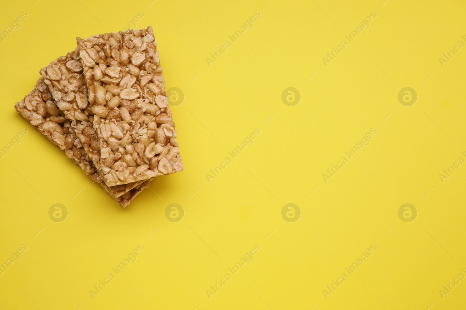 Photo of Tasty peanut bars (kozinaki) on yellow background, flat lay. Space for text