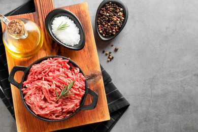 Raw ground meat in bowl, spices, rosemary and oil on grey table, top view. Space for text