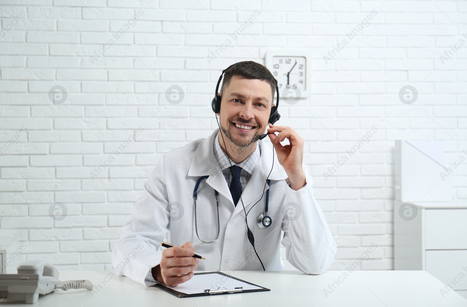 Photo of Doctor with headset sitting at desk in clinic. Health service hotline