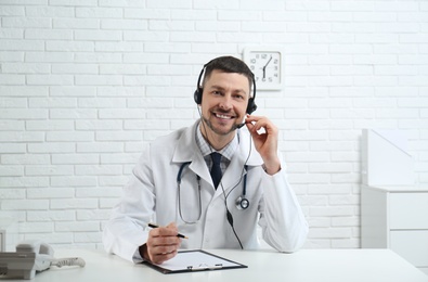 Photo of Doctor with headset sitting at desk in clinic. Health service hotline