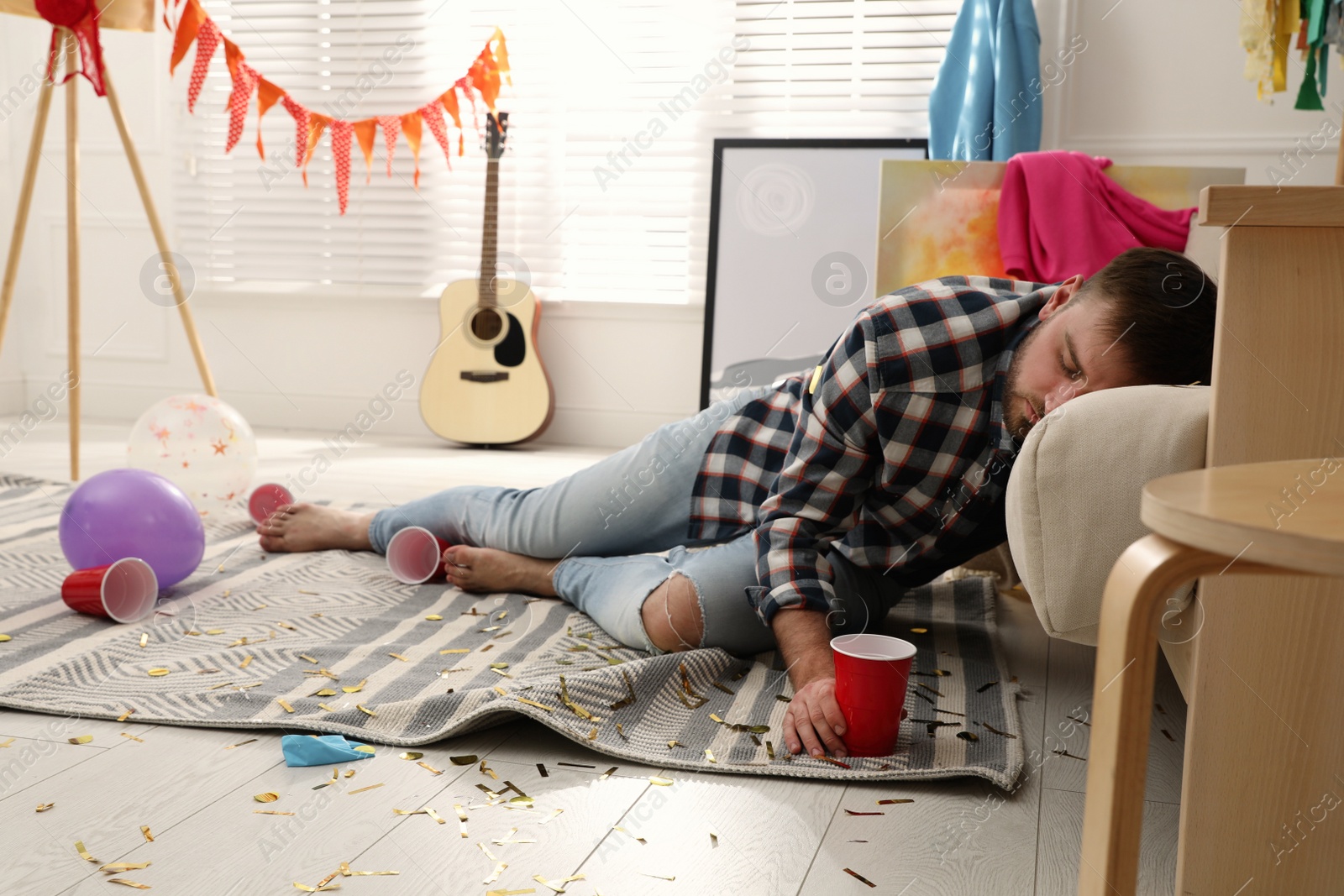 Photo of Young man sleeping near sofa in messy room after party