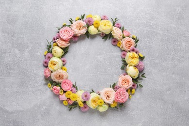 Wreath made of beautiful flowers and green leaves on light grey background, flat lay. Space for text