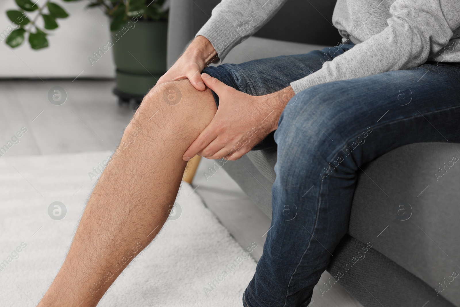 Photo of Man suffering from leg pain on sofa indoors, closeup