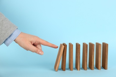 Photo of Woman causing chain reaction by pushing domino tile on light blue background, closeup