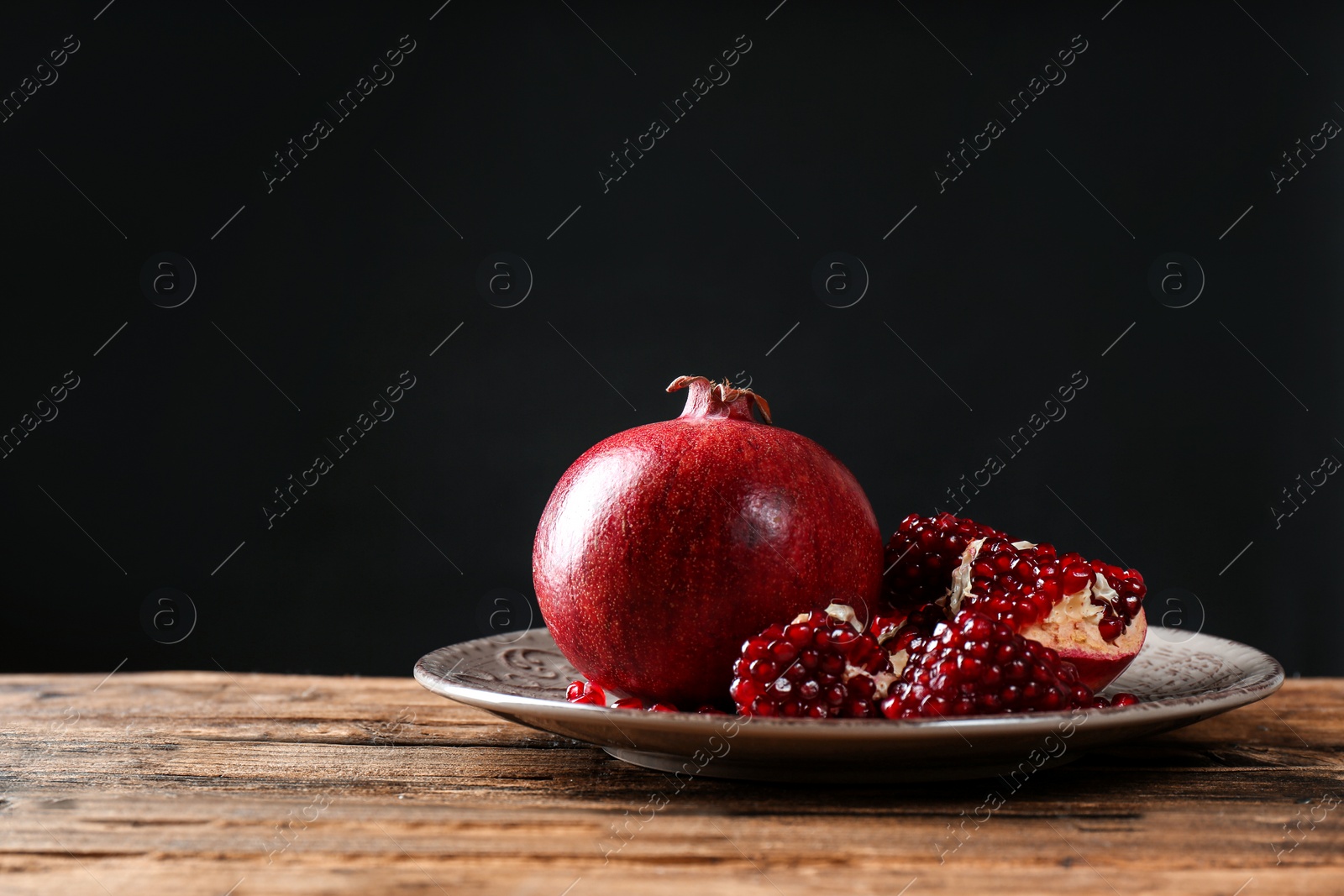 Photo of Plate with ripe pomegranates on table against black background, space for text