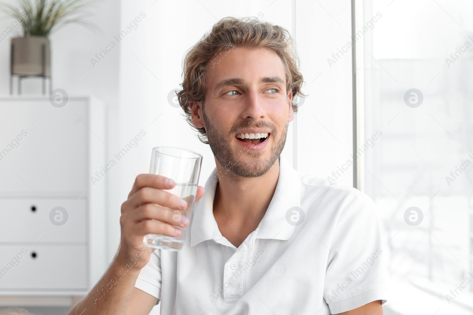 Photo of Young man holding glass of clean water indoors