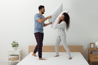 Happy couple having pillow fight on bed with comfortable mattress at home