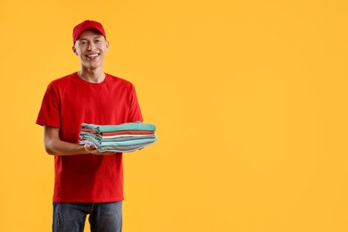 Dry-cleaning delivery. Happy courier holding folded clothes on orange background, space for text