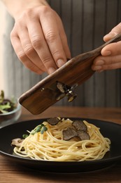 Photo of Woman slicing truffle onto spaghetti at wooden table, closeup