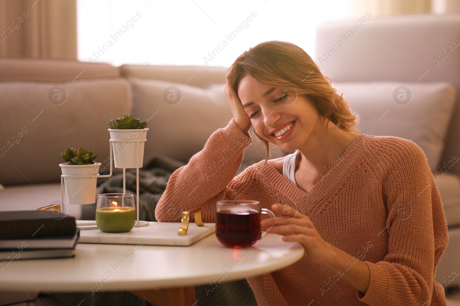 Photo of Beautiful young woman with cup of tea relaxing at home. Cozy atmosphere