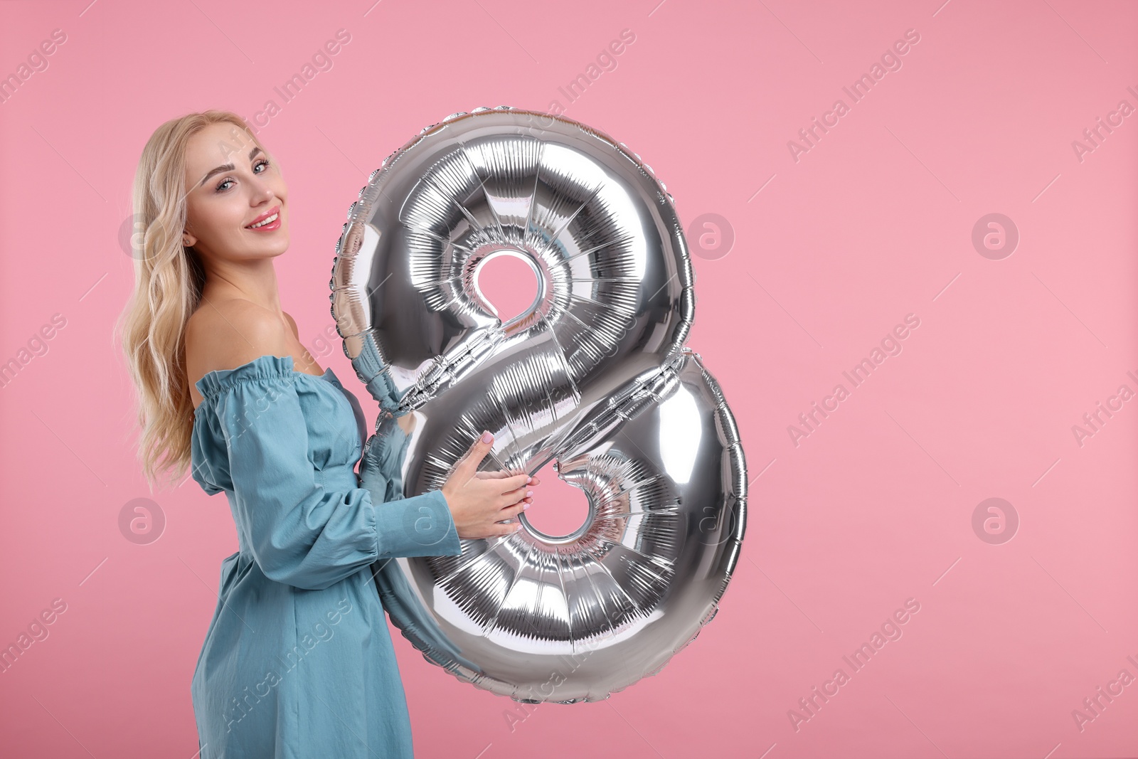 Photo of Happy Women's Day. Charming lady holding balloon in shape of number 8 on dusty pink background