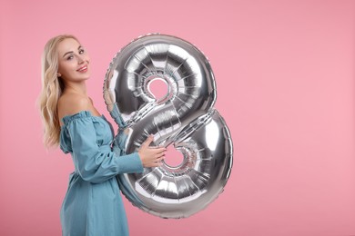 Happy Women's Day. Charming lady holding balloon in shape of number 8 on dusty pink background