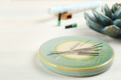 Photo of Light green stone coaster with acupuncture needles on white wooden table, closeup. Space for text