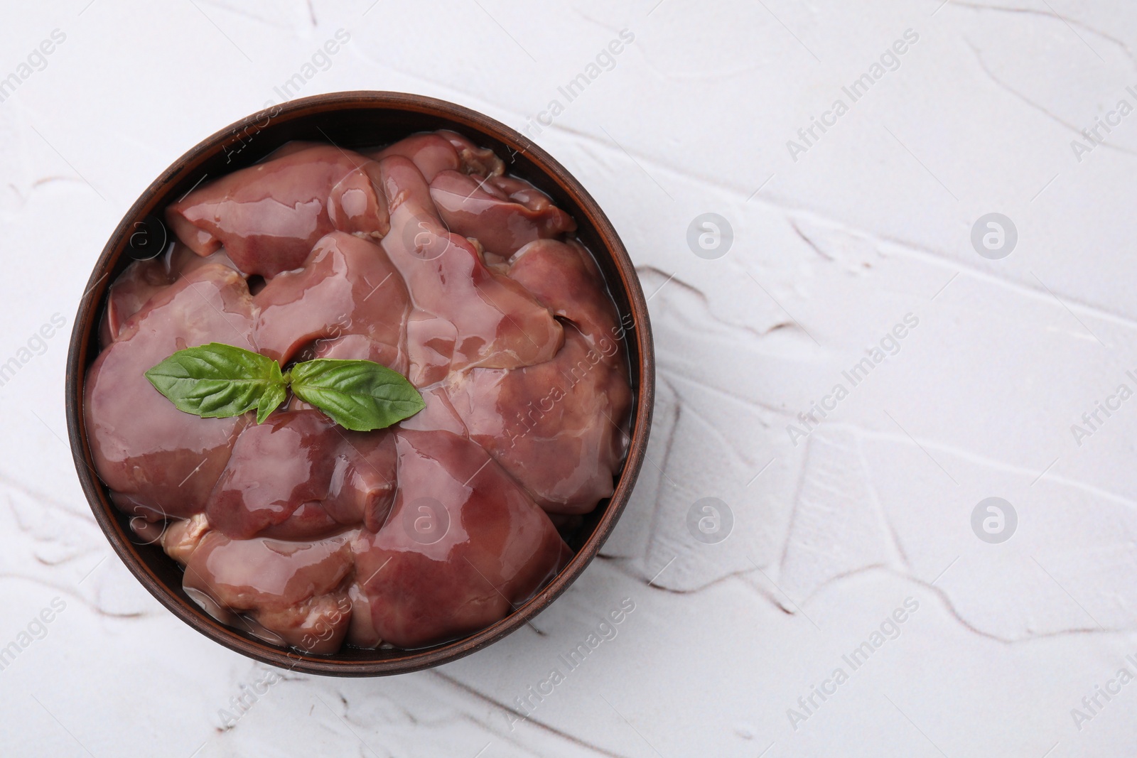Photo of Bowl with raw chicken liver and basil on white textured table, top view. Space for text