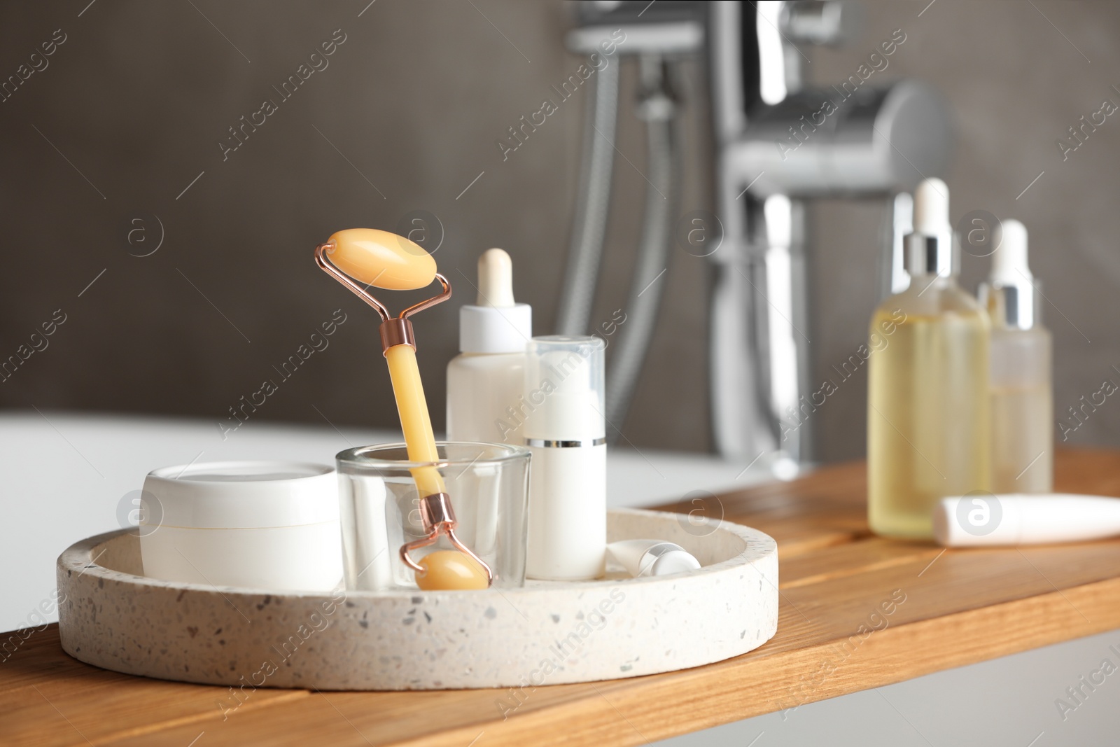 Photo of Bath tray with natural face roller and cosmetic products on tub