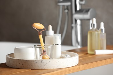 Bath tray with natural face roller and cosmetic products on tub