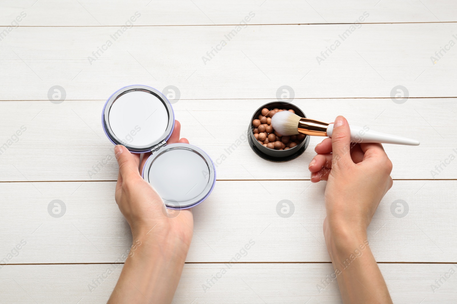 Photo of Woman with stylish cosmetic pocket mirror, blusher and brush at white wooden table, top view